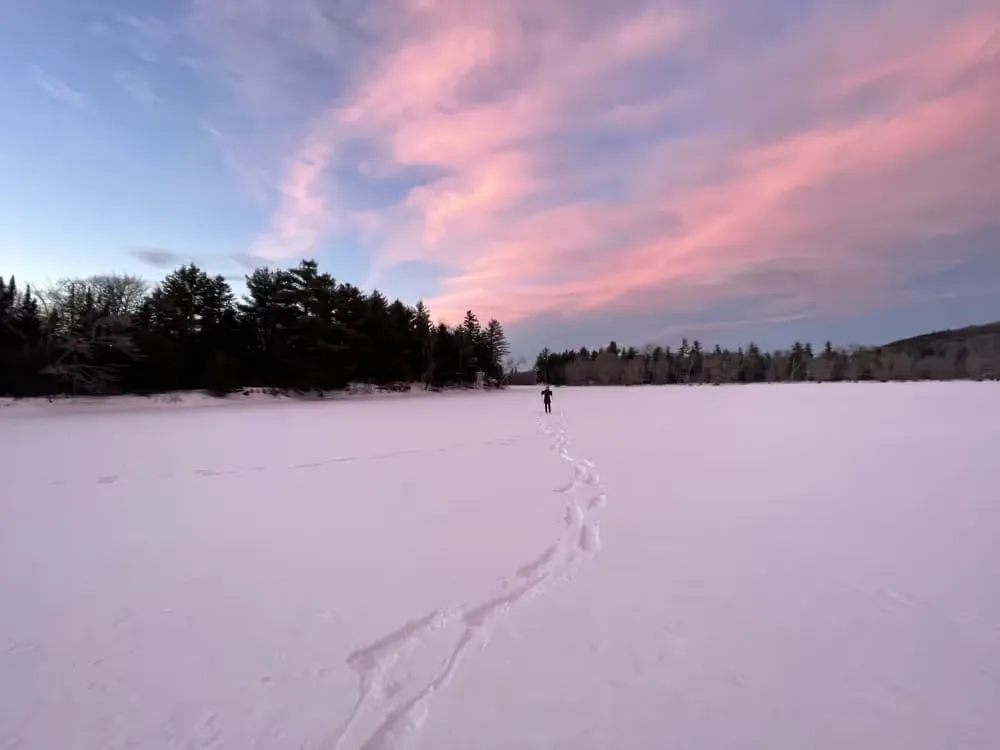 Footprints across a snow-covered frozen lake under a pink sky